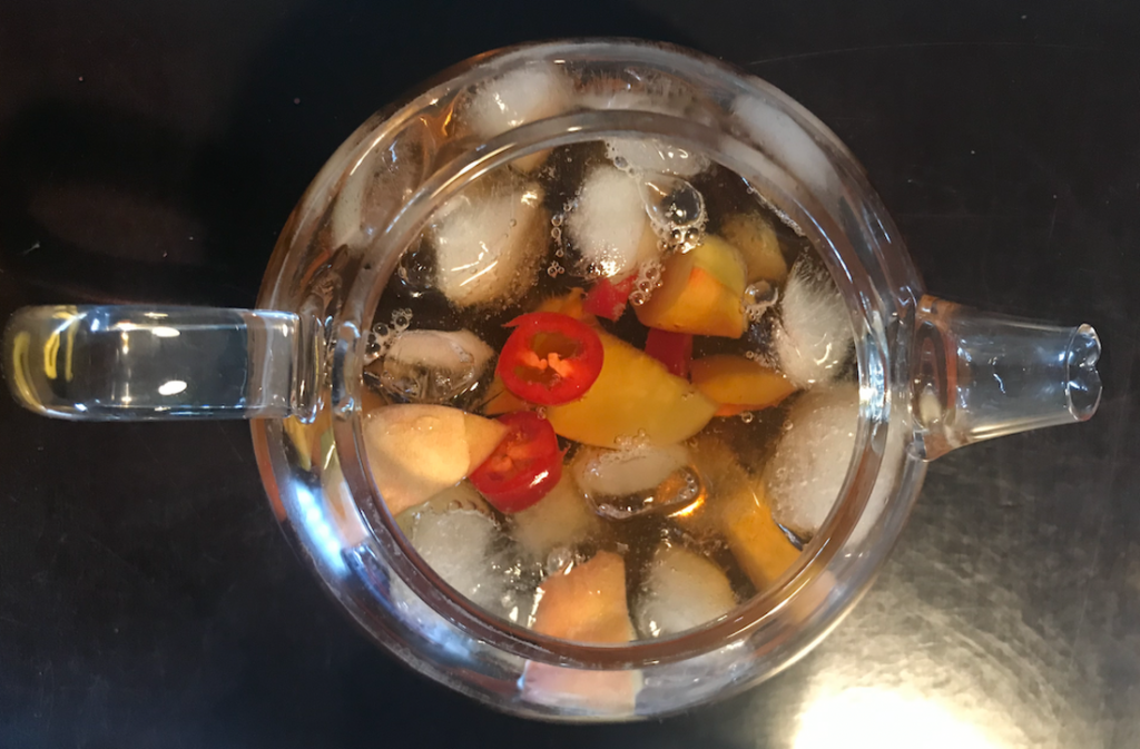 Glazen kan met zelfgemaakte ijsthee, stukjes fruit en een rode peper